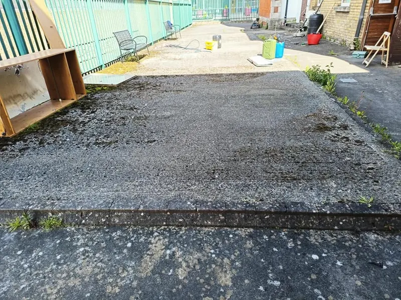 Concrete yard dark with moss and weeds along the edges